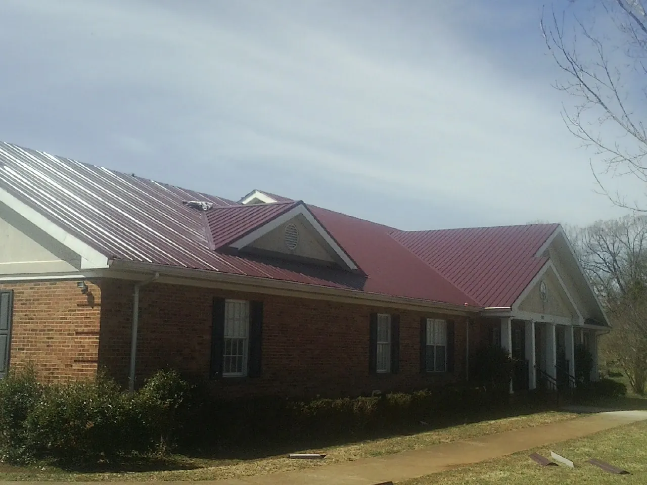 Red metal roof with gabled entries on a long brick building, from a Hail Damage Roof Repair job in New Holland
