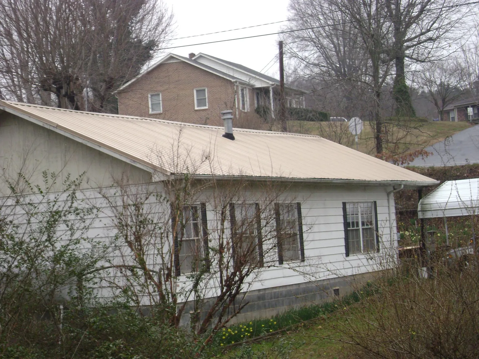 Tan metal roof on a white sided house set into a hillside — Commercial Roofing by Roofing Brothers in New Holland